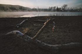 Photo of a lakeside landscape with fog rising from water. Three large logs in the foreground